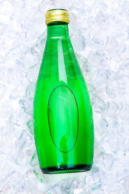 Green bottle of water on ice cubes