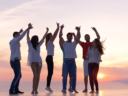 group of happy young people dancing and have fun on party in modern home bacony with sunset and ocean in background