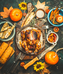 Roasted whole stuffed chicken or turkey for Thanksgiving Day , served with sauce, pumpkins, corn and autumn harvest vegetables, kitchen knife and cutlery on dark rustic background, top view