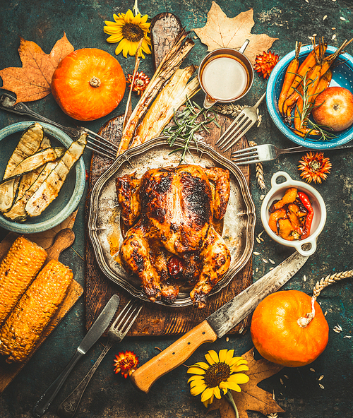 roasted whole stuffed chicken or turkey for thanksgiving day , served with sauce, pumpkins, corn and autumn harvest , kitchen knife and cutlery on dark rustic background, top view