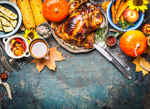 Festive  Thanksgiving Day food background with roasted whole turkey or chicken and sauce, harvest vegetables: corn, pumpkin,carrots with cutlery on dark rustic kitchen table, top view, border