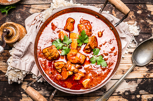 Goulash or stew in vintage pot with tomtoes sauce on rustic wooden background, top view