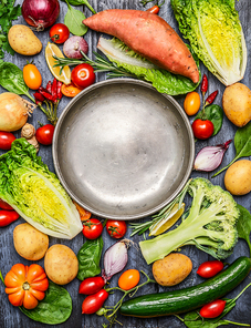 Fresh colorful organic season vegetables ingredients around empty steel  plate on rustic wooden background, top view, copy space. Healthy, diet or vegetarian food concept.