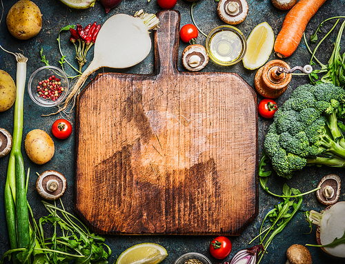 Fresh vegetables and  ingredients for cooking around vintage cutting board on rustic background, top view, place for text.  Vegan food , vegetarian and healthily cooking concept.