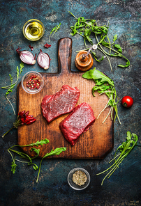 Delicious  beef steak on vintage cutting board with fresh various ingredients for tasty cooking on rustic wooden background, top view.