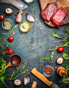 Fresh beef steak, wooden spoon, knife and aromatic herbs, spices and vegetables for cooking , on rustic background, top view, frame.