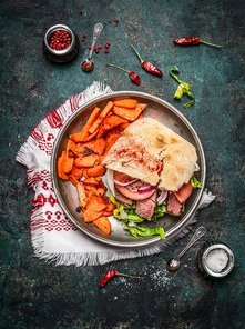 Sandwich with ciabatta bread , roasted meat, vegetables and sweet potato in plate on rustic wooden background, top view