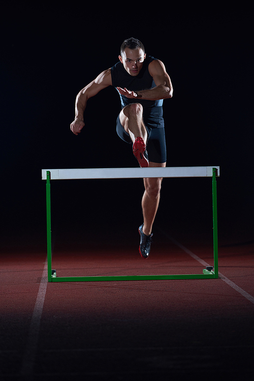 man athlete jumping over a hurdles on athletics race track