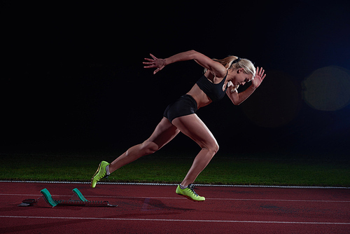 woman  sprinter leaving starting blocks on the athletic  track. Side view. exploding start