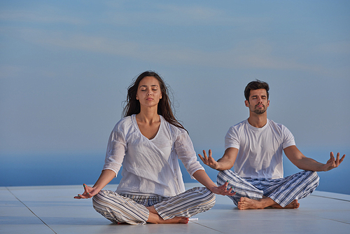 young couple practicing yoga at sunset in modern home terace with ocean and sunset in background