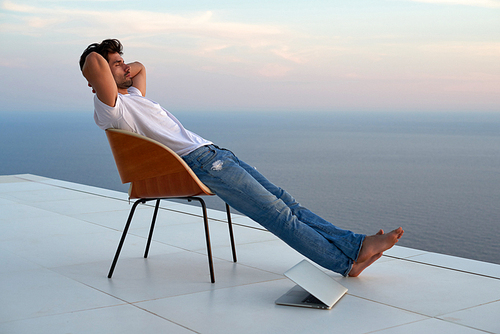 handsome young man relaxing and working on laptop computer at home balcony while looking sunset