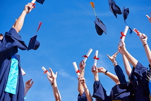 high school students graduates tossing up hats over blue sky.