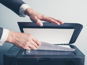 The hands of a young businessman is placeing a document on a flatbed scanner in preperation for copying it
