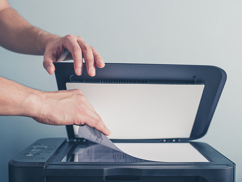 The hands of a young man is placeing a piece of paper on a flatbed scanner in preperation for copying it