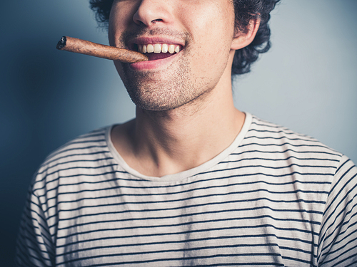 A happy young man in a stripey top is smoking a cigar