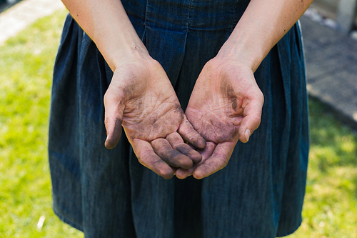 A young woman is showing of her dirty hands covered in dirt from gardening