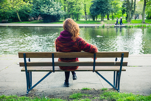 A young woman is sitting and relaxing on a bench in the park by a pond