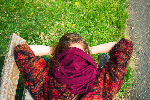 A young woman is sleeping on a bench in the park with a scarf covering her face