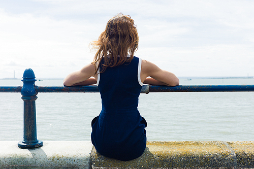 A young woman is sitting by a railing on a promenade by the seaside