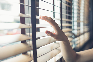 A young female hand is touching some venetian blinds by the window