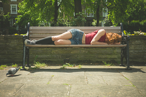 A young woman is lying down and relaxing on a park bench on a sunny  summer day