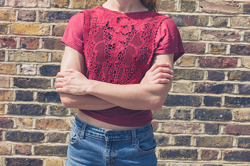 A young woman wearing a red top is standing in the street by a brick wall