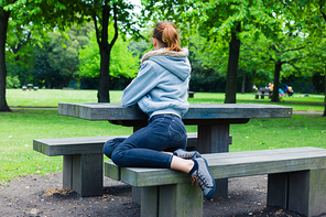A trendy young woman is sitting on a bench by a table in the park