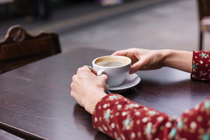 The hands of a young woman with a cup of coffee on a table outside in the street