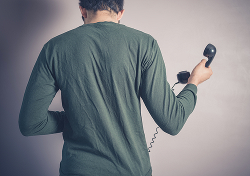 Rear view shot of a young man using a vintage rotary telephone