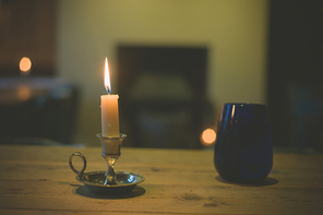 A lit candle and a blue glass on a table in a dining room