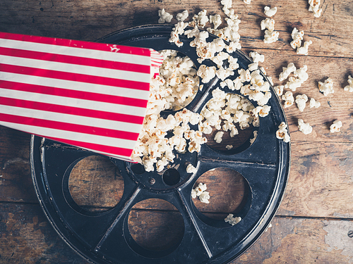 Cinema concept of vintage film reel with popcorn on wooden surface