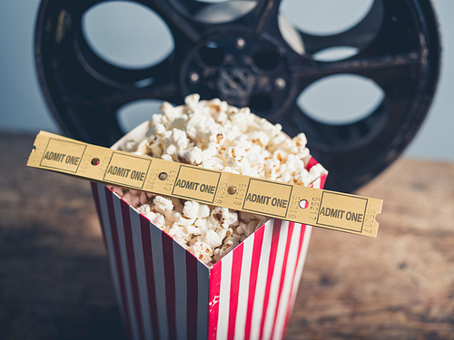 Cinema concept of old film reel with popcorn and movie tickets on a wooden surface