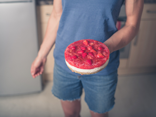 A young woman is standing in a kitchen with a freshly baked strawberry cheesecake