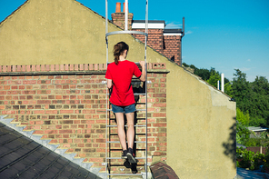 A young woman is climbing a ladder on a roof