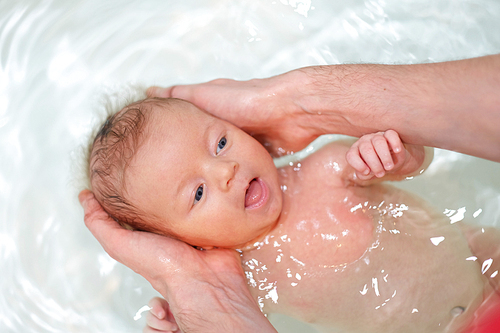 Newborn baby swimming in bath with help of father's hands