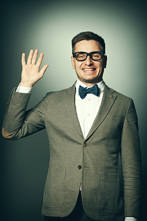 Nerd in eyeglasses and bow tie says Hello against grey background