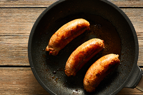 Fried sausages on frying pan over wooden background