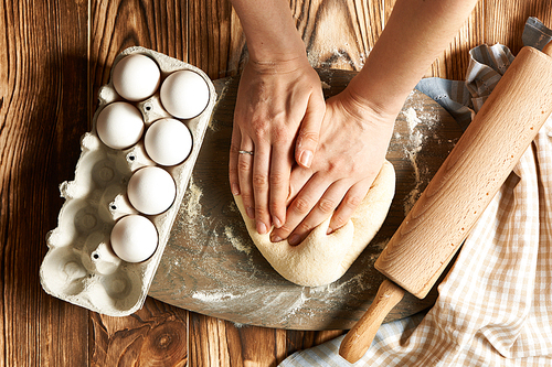 Female hands kneading dough on wooden table