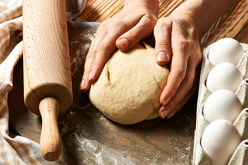 Female hands kneading dough on wooden table