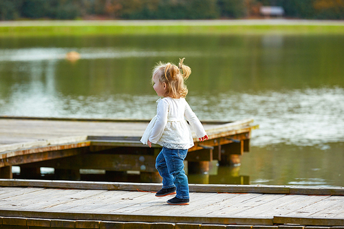 Blond Kid girl walking in the lake pier at the park
