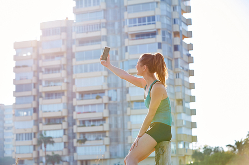 Runner girl having a rest shooting selfie with smartphone outdoor building park