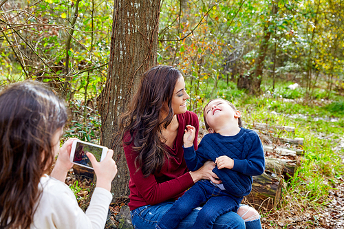 daughter taking mobile photo of mother and son brother in the park having fun