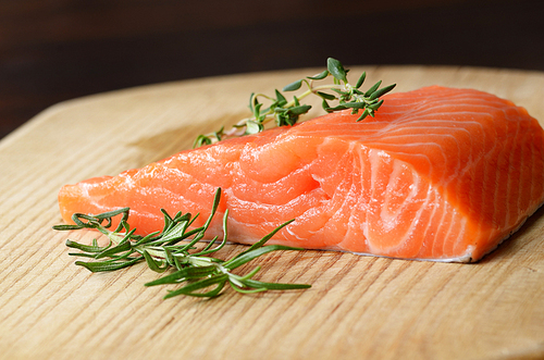 Raw salmon fillet with rosemary on wooden cutting board