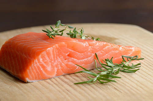 Raw salmon fillet with rosemary on wooden cutting board