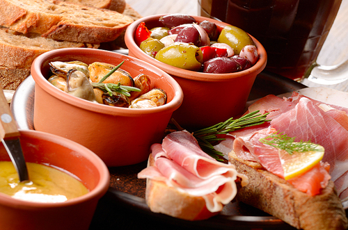 Tapas of salmon, mussels, jamon and olives on ceramic plate with glass of beer aside