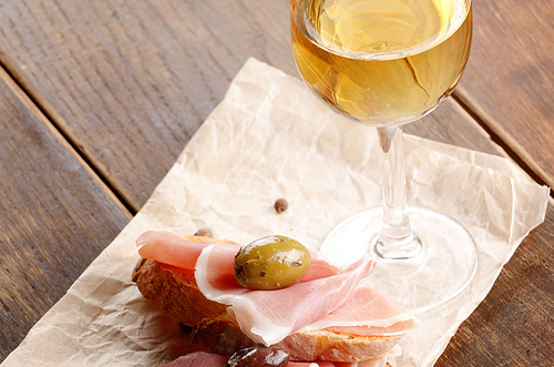Open jamon sandwiches with white wine on wooden table