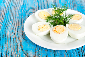 Boiled hen eggs and green dill in a white plate on a blue wooden background