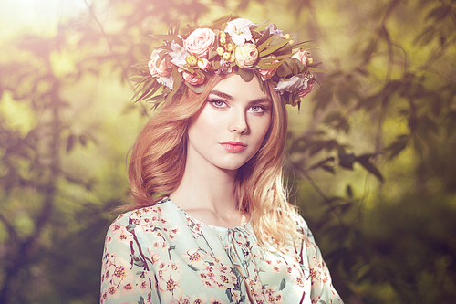 Beautiful blonde woman with flower wreath on her head. Beauty girl with flowers hairstyle. Girl in a summer forest. Fashion photo