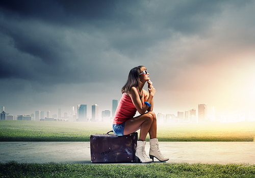 Young pretty girl traveler sitting on suitcase aside of road