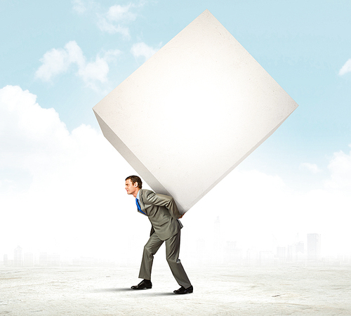 Image of businessman carrying big white cube on his back